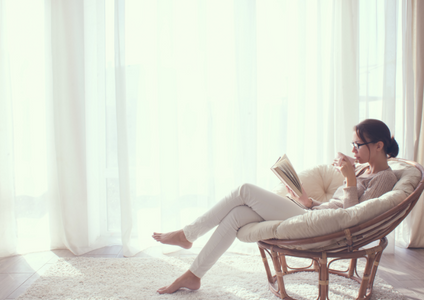 A relaxed woman enjoys a warm coffee and a book in her tranquil, organised living room. This image represents the total peace of mind achieved with Storage King's full service concierge, which handles the entire decluttering process, including removalists, boxes, packing supplies, and self storage.